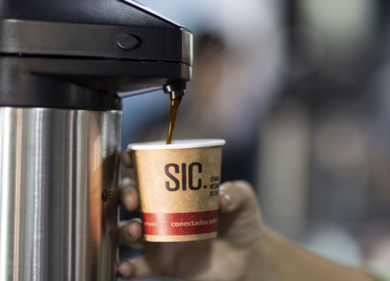 Uma mão segurando um copo com a marca do evento SIC