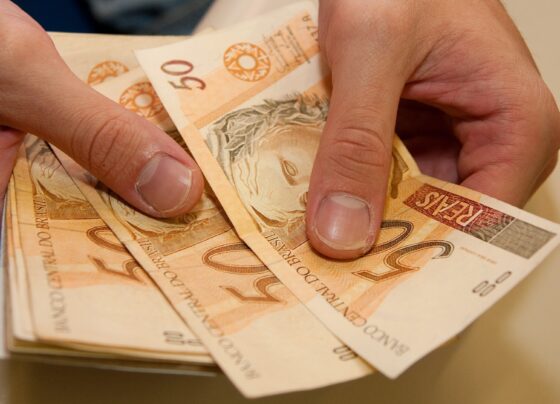 mãos segurando notas de cinquenta reais auxílio emergencial renda mínima crédito