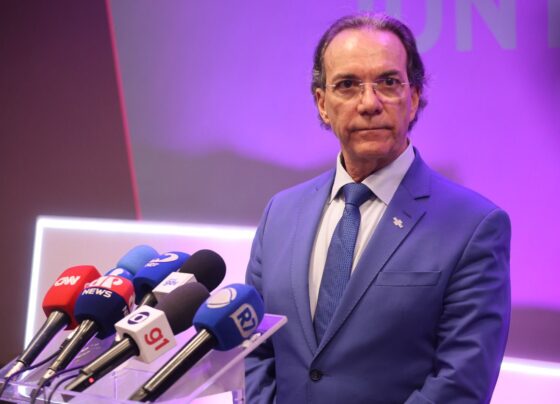 Homem em pé com terno azul e fundo neutro