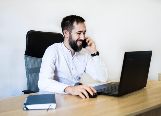 Homem sentado em uma cadeira, sobre a mesa há um notebook e uma agenda